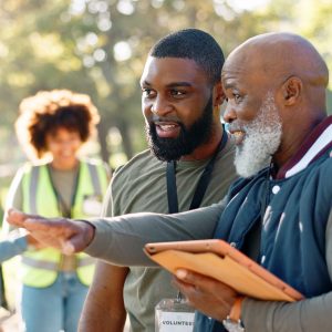 Two Black men, one older and one younger, discussing a park cleanup project while standing outdoors